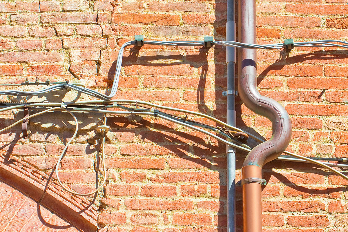 Electrical power cables and telephone cables against an old brick wall.