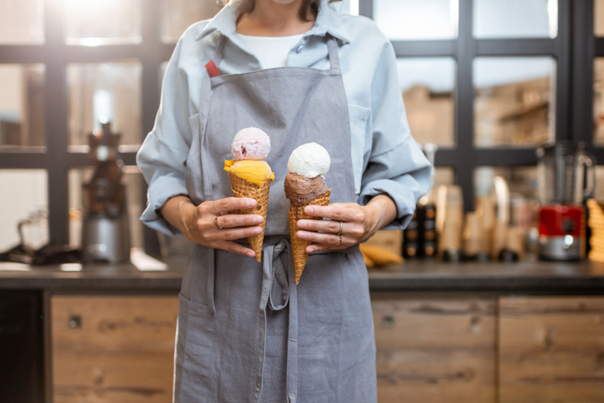 Female seller holding two yummy ice creams in waffle cone at the shop close up.