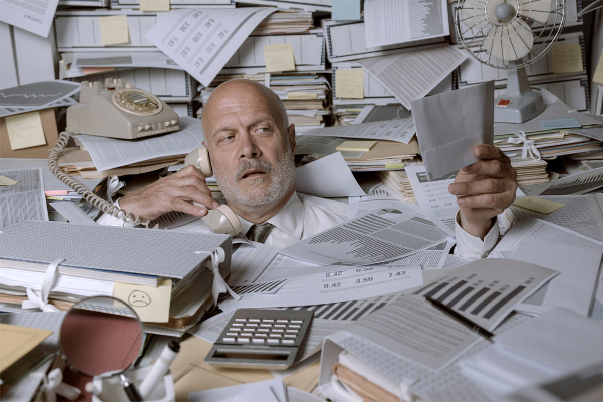 Stressed businessman overwhelmed by work he is drowning under a lot of paperwork and answering phone.