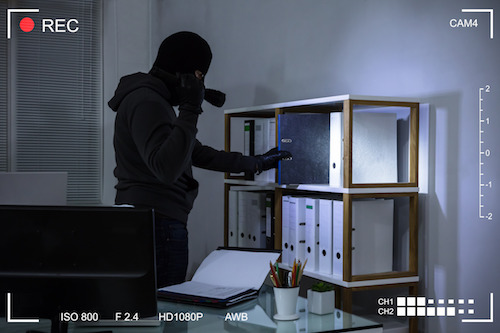 Thief wearing balaclava stealing file from shelf at workplace scene through cctv camera.