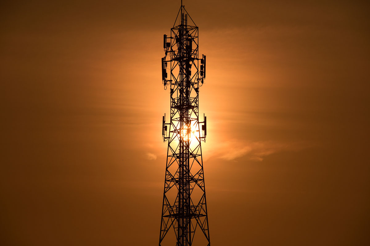 Wireless communication/telecommunication tower with antennas against sunset background.